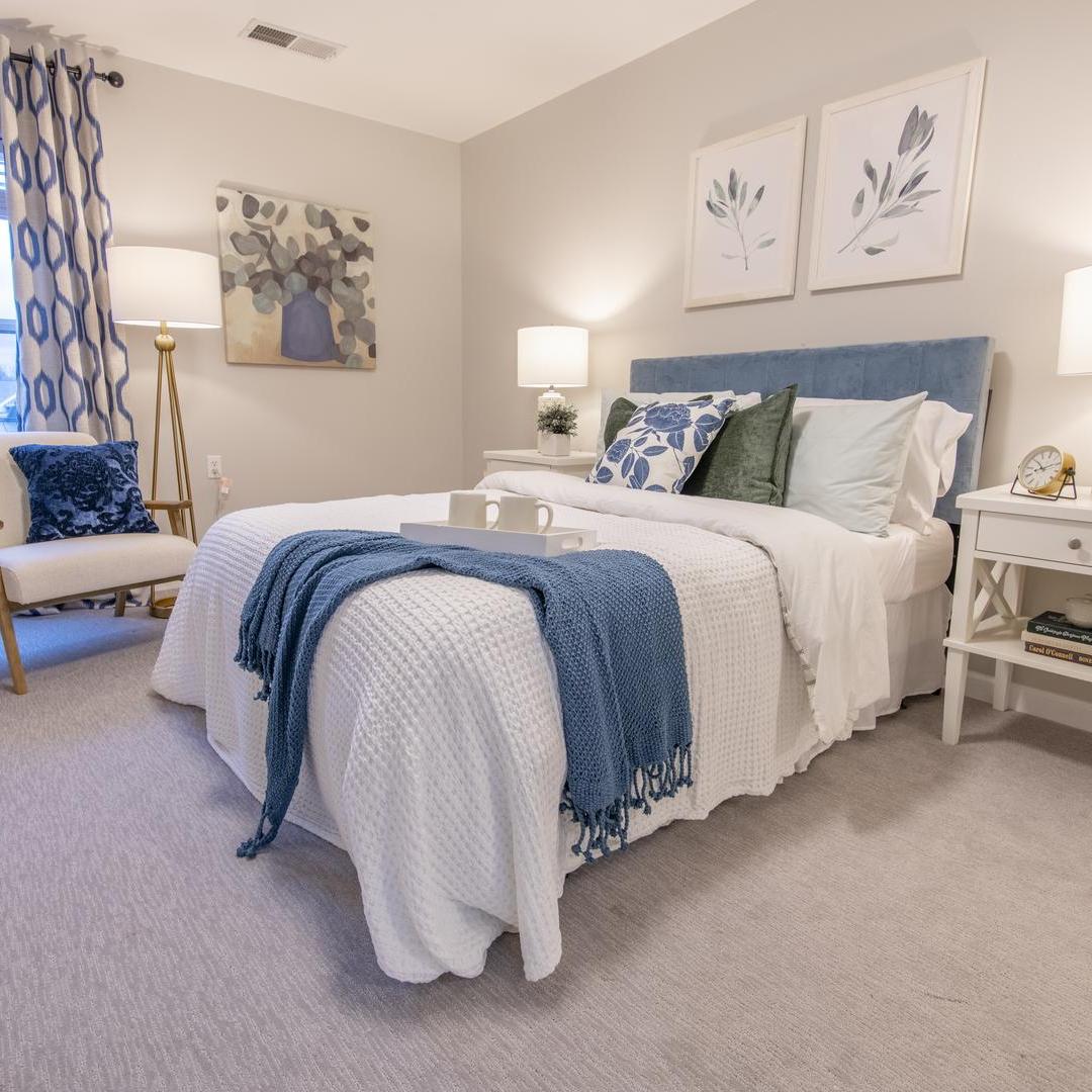 A fully furnished bedroom with white comforter and blue throw at end of bed.