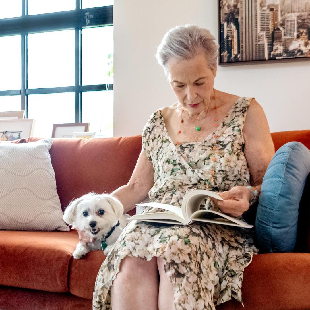 A resident on an orange couch sitting next to small white dog.