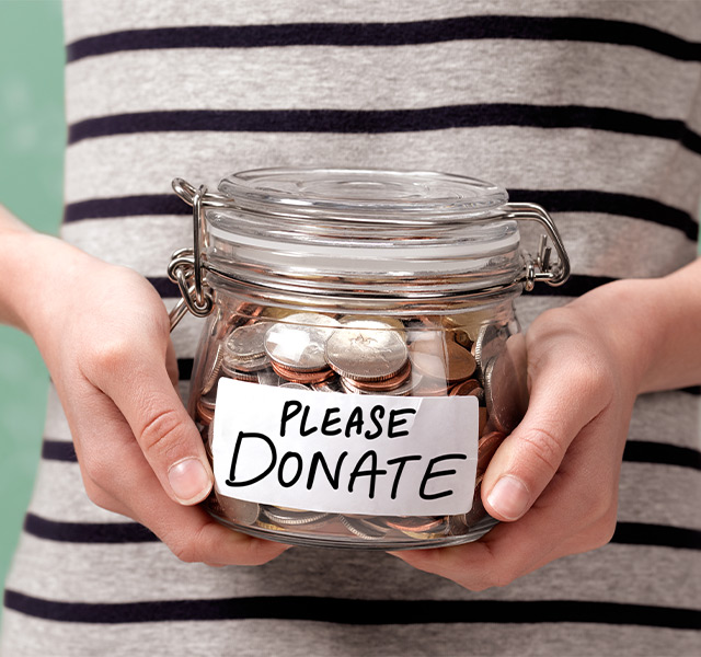A person holding a jar of change that says please donate.