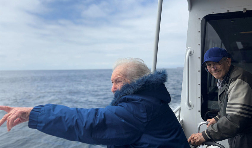 Two people on a boat pointing out into the ocean.