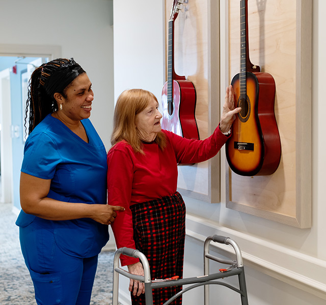 A person with a caregiver touching guitars on the wall.