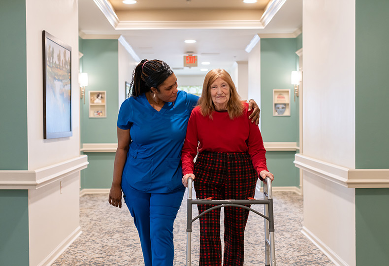 A caregiver helping a person walk in the hall.