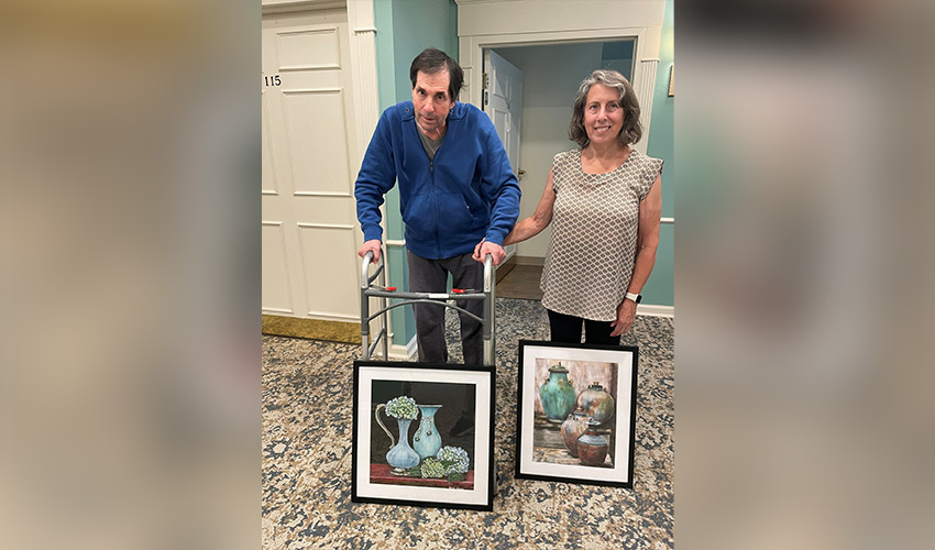 Two people standing with paintings.