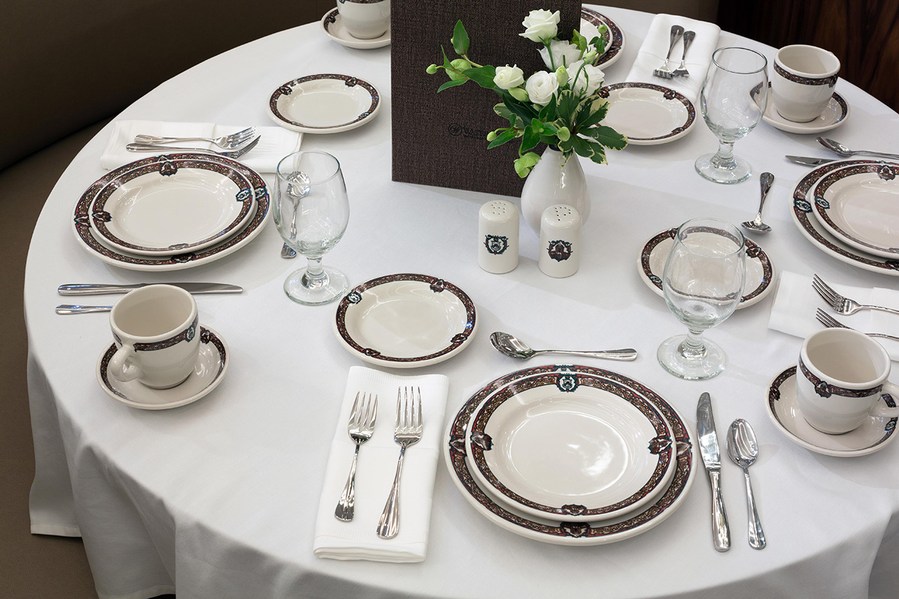 Round table with set plates, cutlery, and glasses.