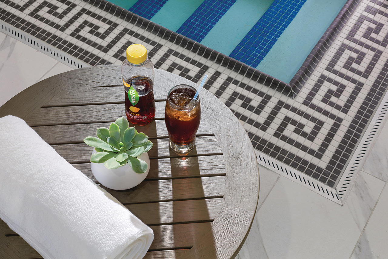 Table stand by pool holding a plant and dinks and a towel.