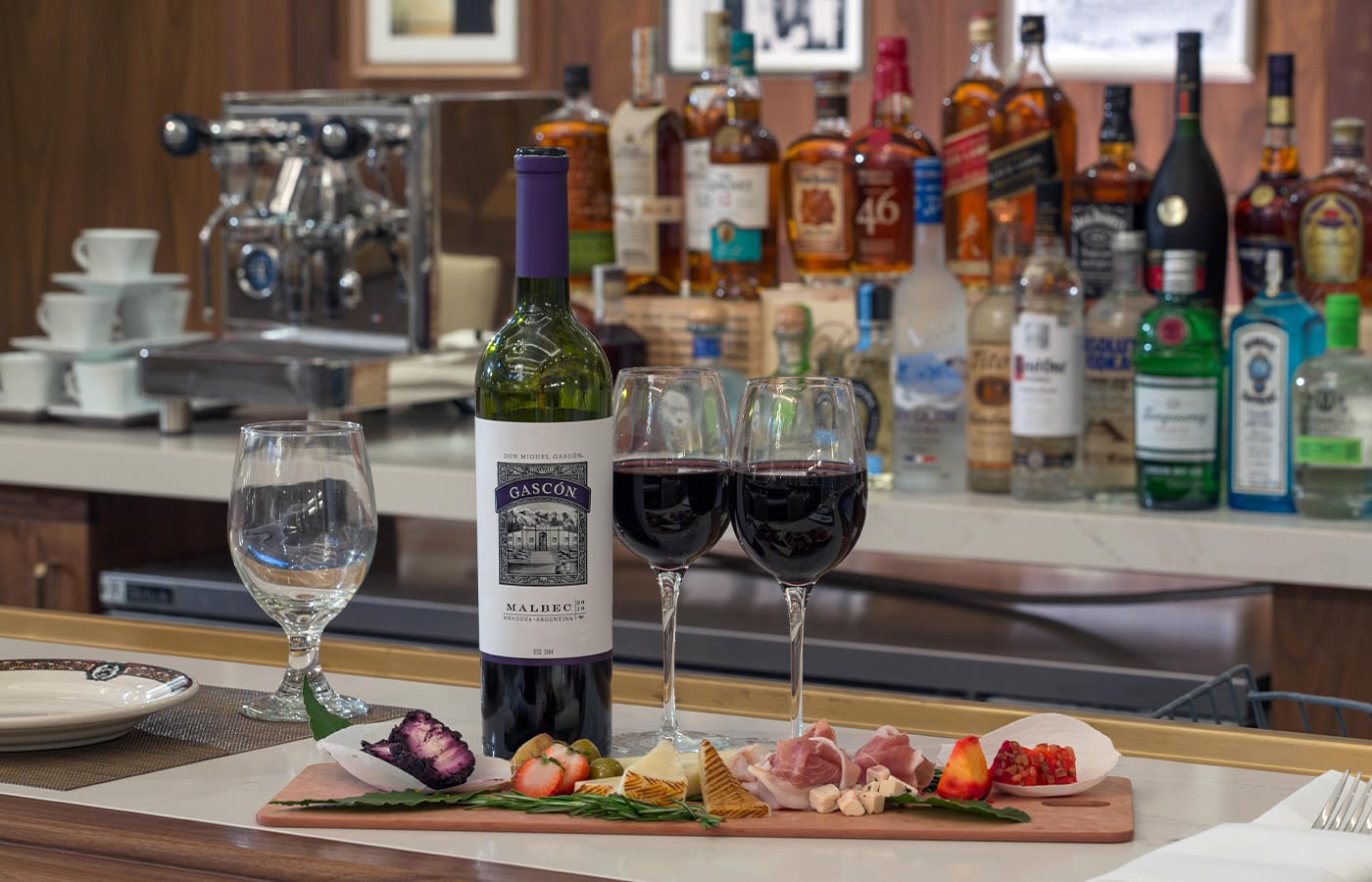 Wine and cheese pairing set atop a bar top showcasing a variety of spirits in the background.