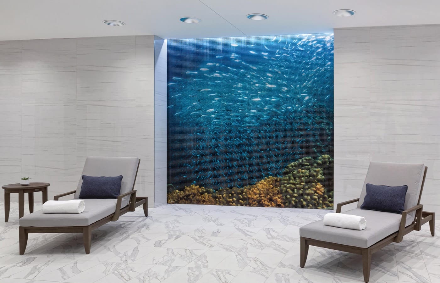 Lounge chairs found at the indoor pool space placed in front of a mosaic mural depicting the view from the sea floor looking upwards.