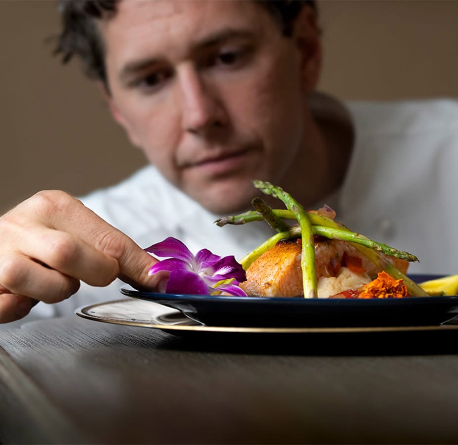 A chef placing a decorative flower on the edge of a meal to enhance the presentation.