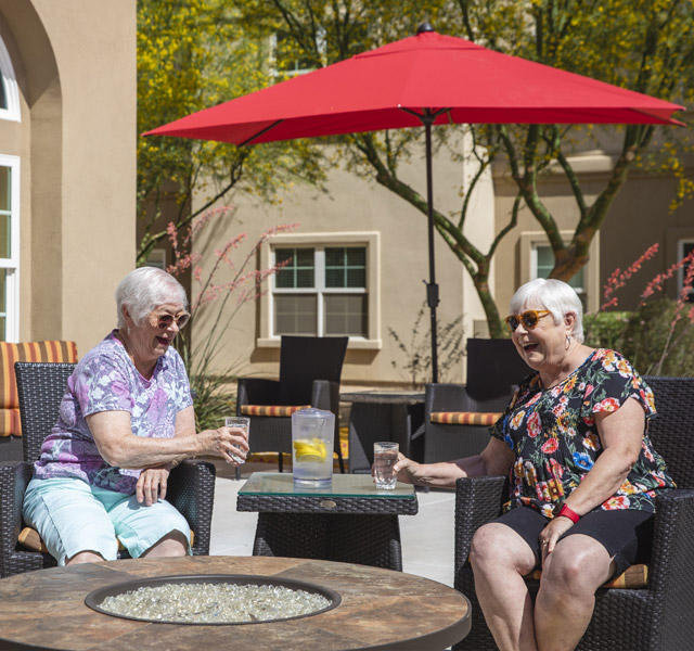 Two residents chatting and sitting on the patio under a large red umbrella.