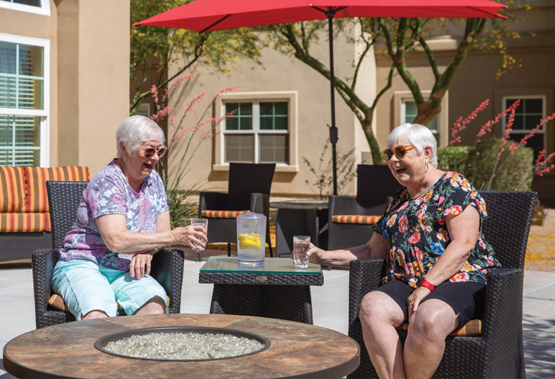 Two residents chatting and sitting on the patio under a large red umbrella.