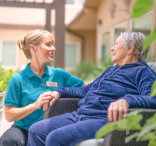 A resident is seated chatting with a caregiver outside.