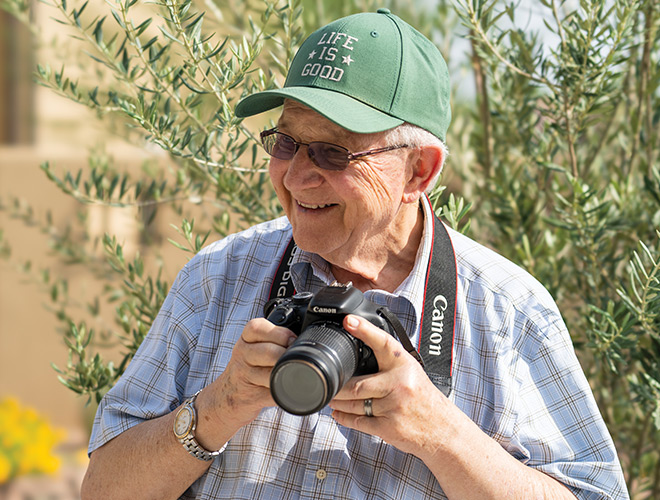 A person wearing a green baseball cap and holding a camera outside.