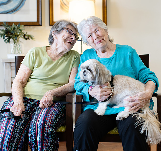 Two residents sitting down holding a dog.