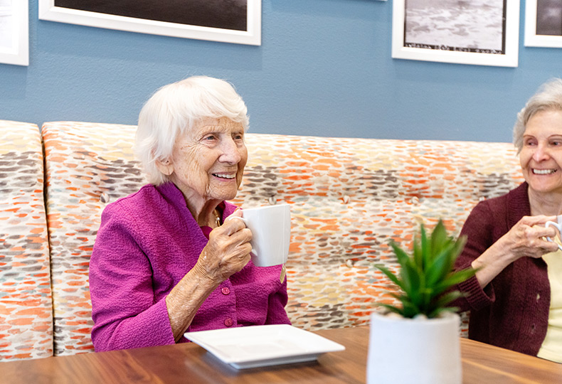 Two residents smiling and drinking coffee in casual colorful dining area.