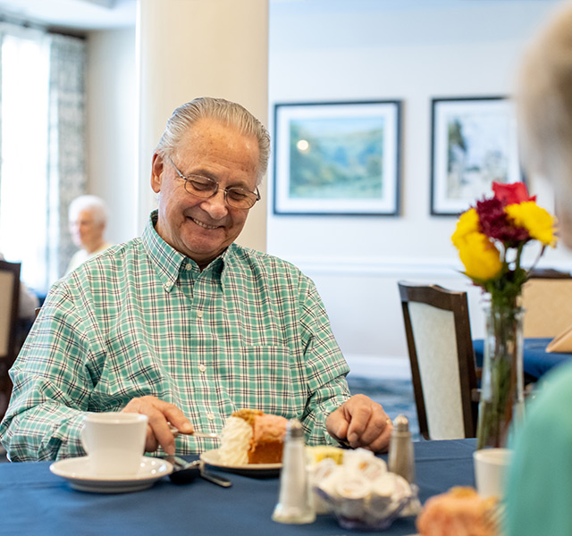 A resident is enjoying a pastry and coffee with another resident.