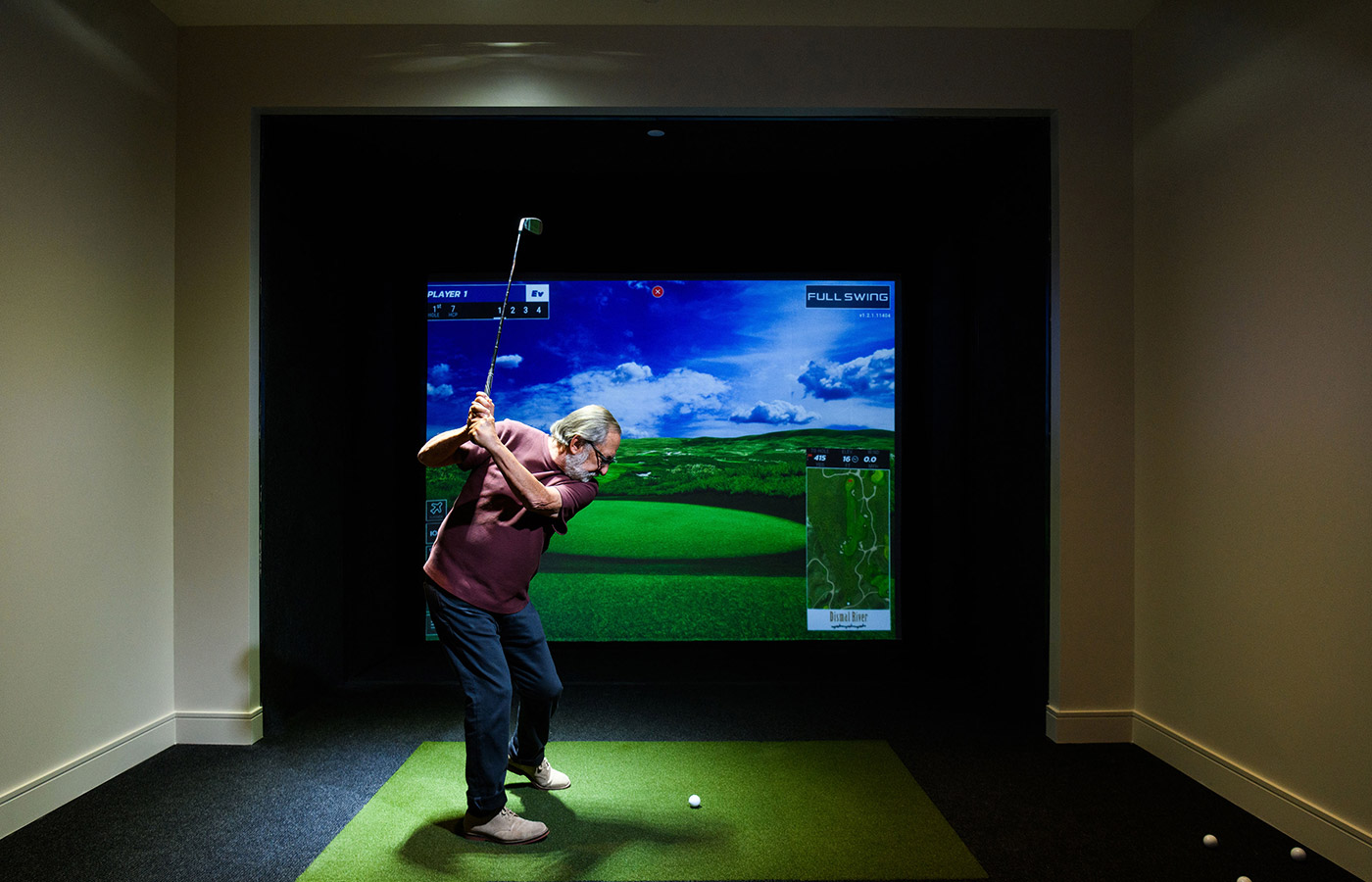 A resident is playing golf in the indoor interactive golf area.