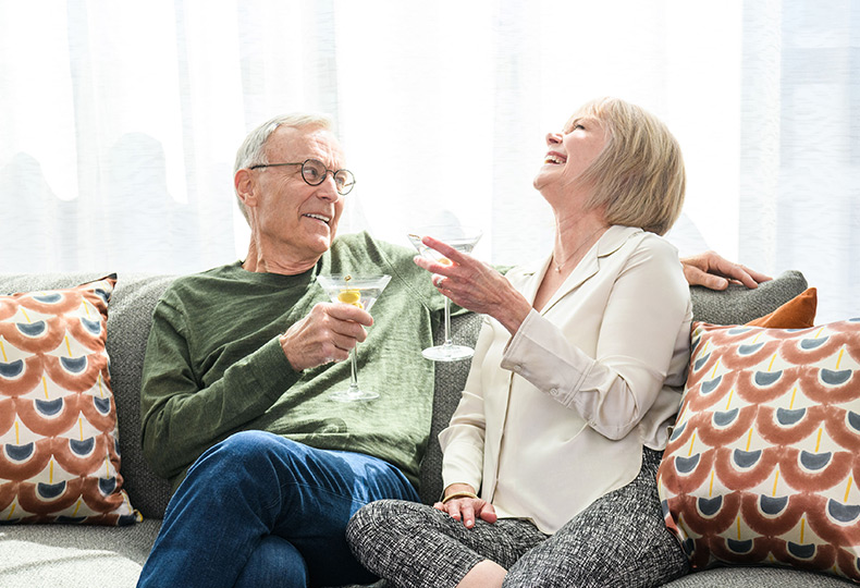 A resident couple sitting on the couch with drinks, laughing.