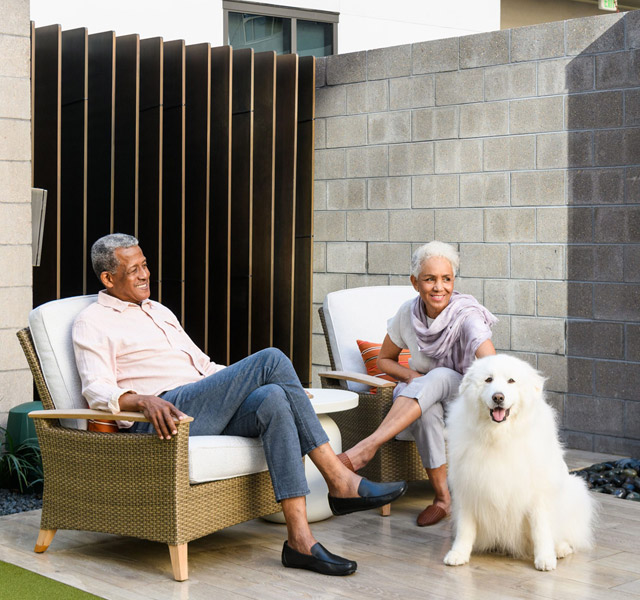 Two residents are sitting on the patio behind a large fluffy dog.