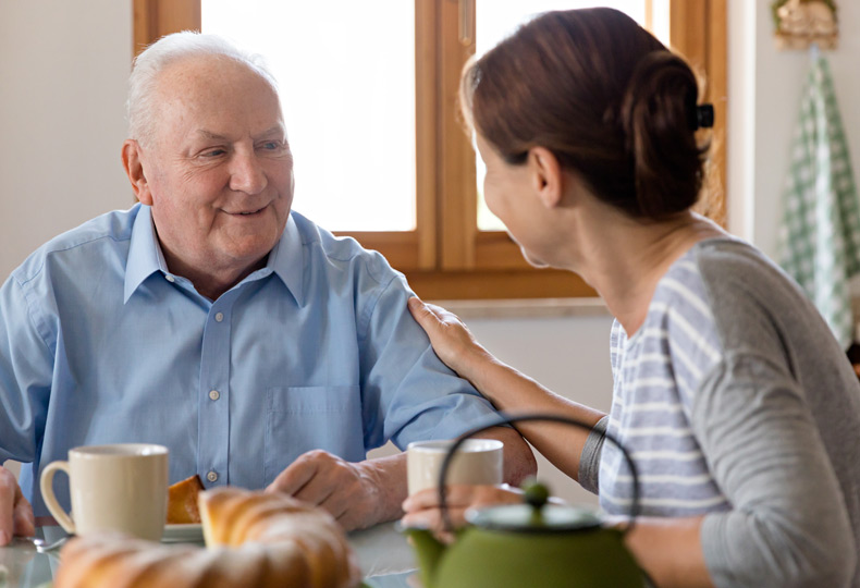 A caregiver has their hand on a resident whilst having a conversation at breakfast.