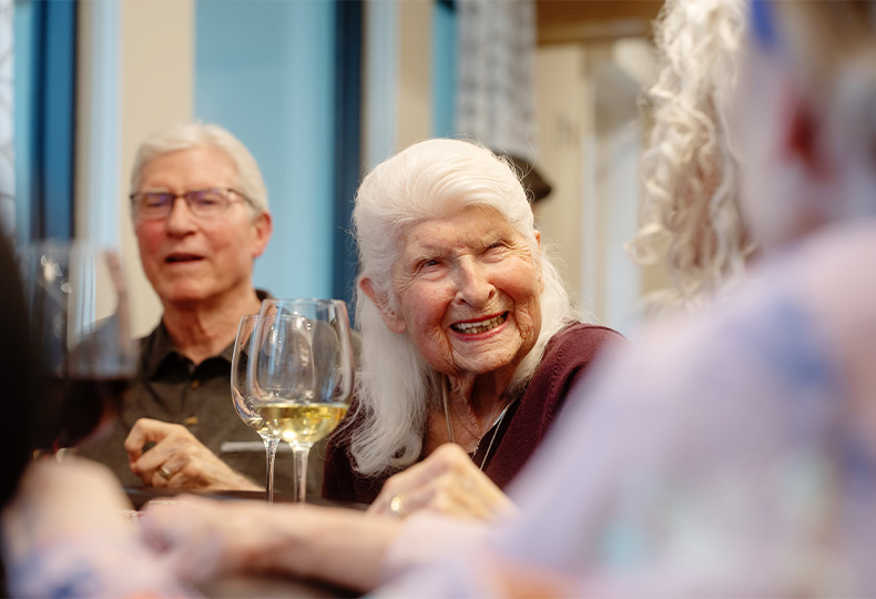 A person smiling at a table with wine.