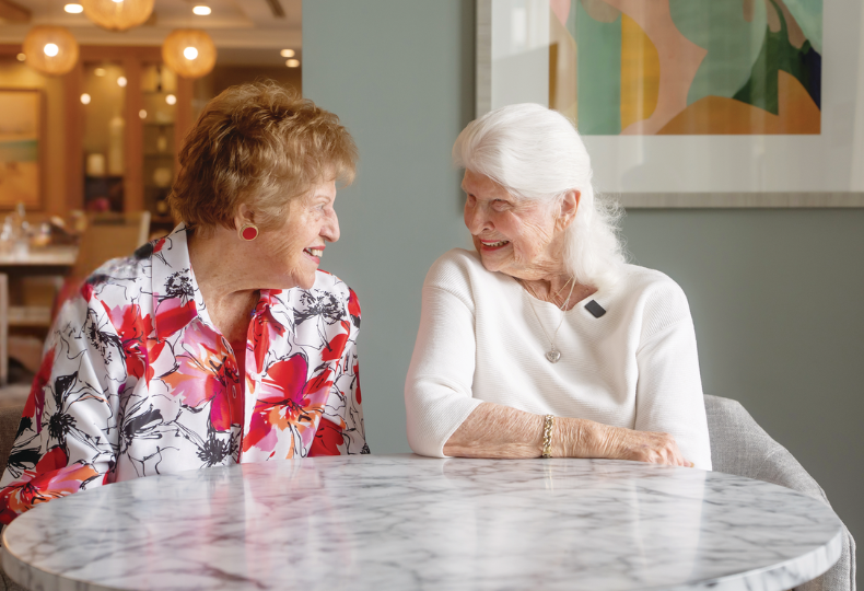 2 people smiling at each other sitting at table.