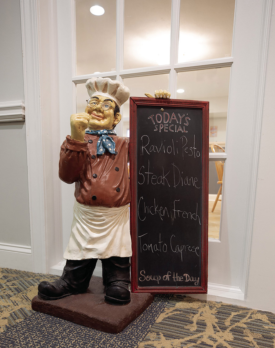 A chef statue holding a chalk board with menu items written on it.