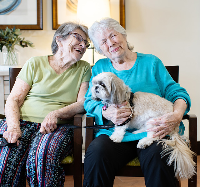 Two residents are sitting and holding a dog.