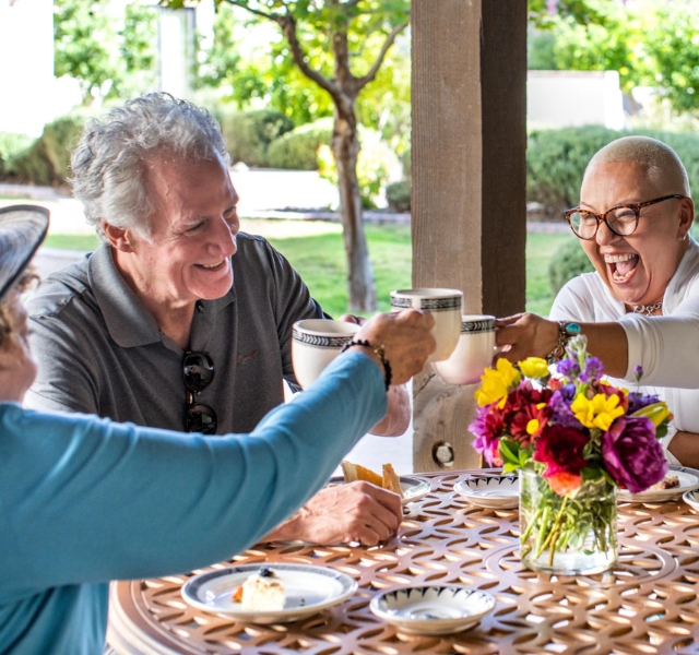 Three friends toasting with coffee mugs and enjoying pastries.