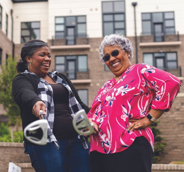 Two people laughing and holding golf clubs.