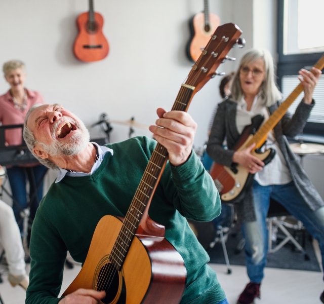A group of people playing music. One person is  rocking out with a guitar.