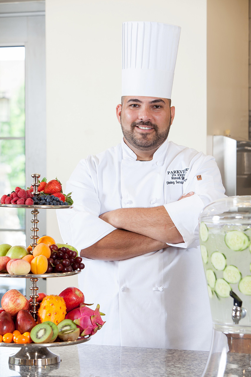 Happy chef next to a tiered platter of fruit.
