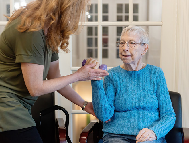 A person helping a resident lift a weight.