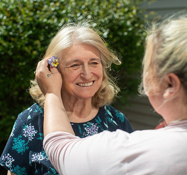 A caregiver putting a flower behind a resident's ear.