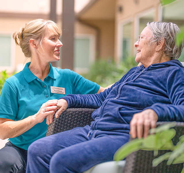 A resident is sitting outside and talking to their caregiver.