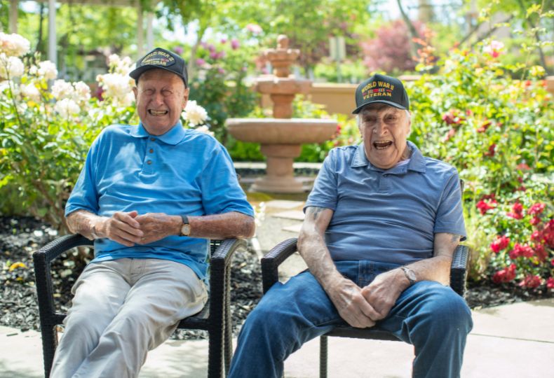 Two veterans are sitting on a bench outside.