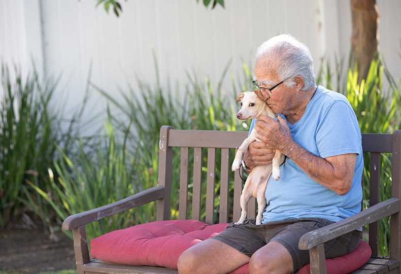 A resident sitting on a bench kissing their little dog.