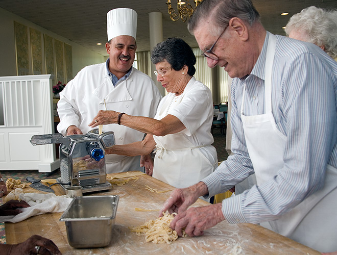Two residents are making pasta in a cooking class alongside the chef.