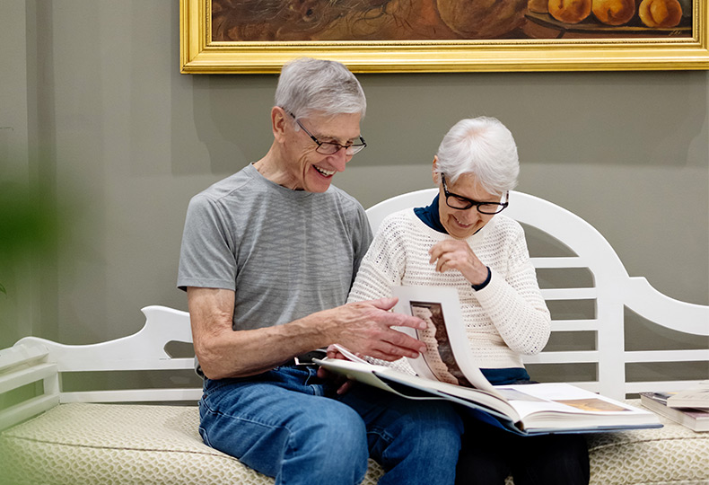 Two people sitting on a bench looking at a book.
