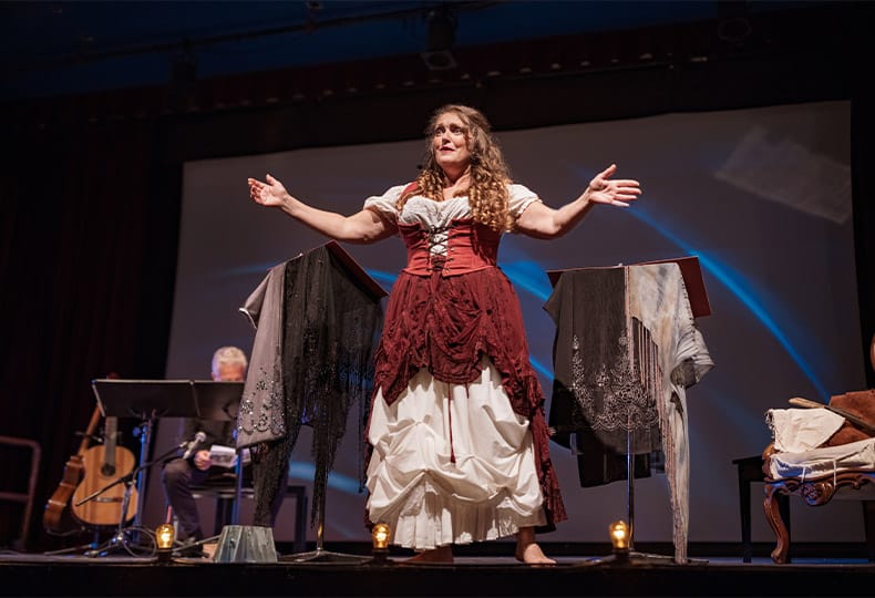 Performer on the stage. She is dressed in period costume. Stage interior of Theatre during performance at night.