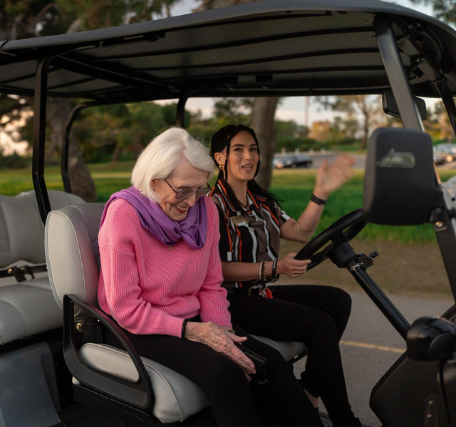 Resident laughing and associate is waving from a golf cart.
