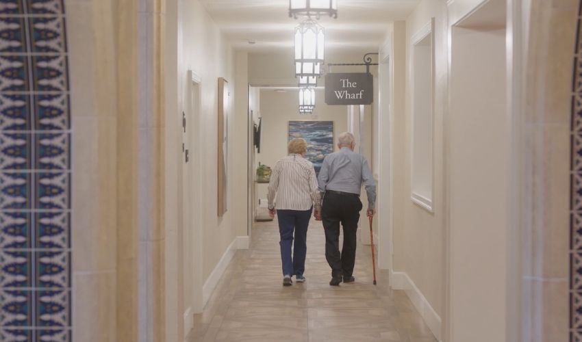 Two residents are holding hands and walking down a hallway.