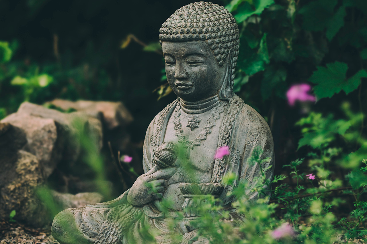 Buddha statue surrounded by trees and flowers.