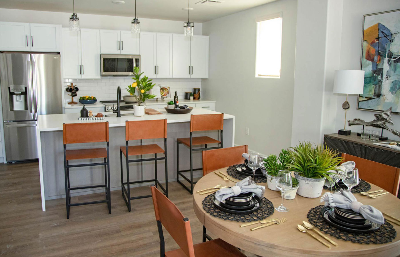 A modern kitchen with white cabinetry, stainless steel appliances, bar height chairs and a dining table in a model residence.