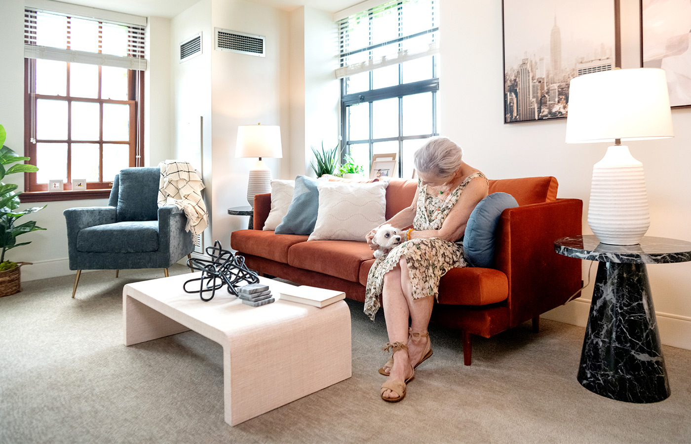 Woman in her furnished living room space with sofa, table, and seating area.
