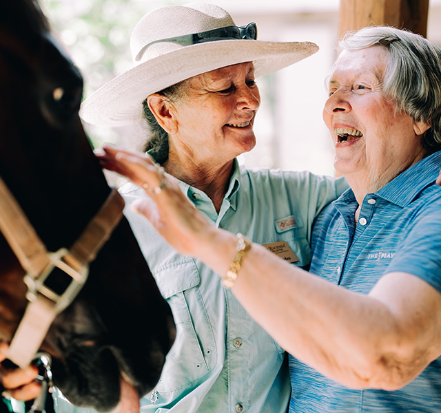 An associate and a resident laughing and petting a black horse.