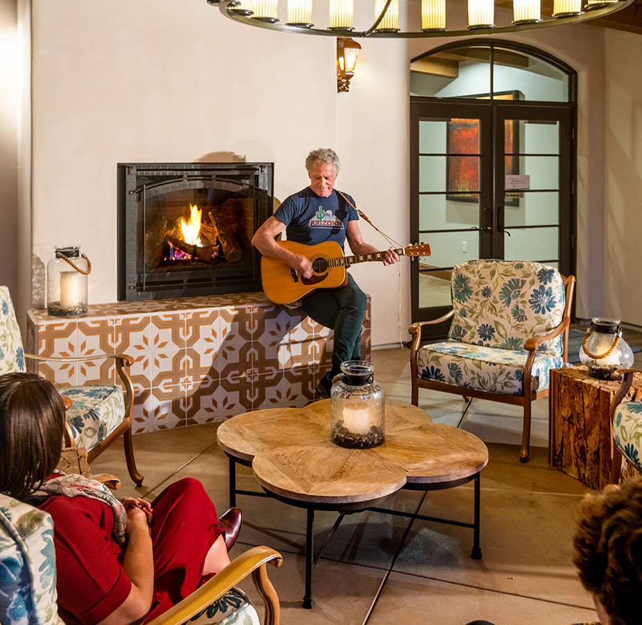 Person playing guitar in seating area in front of people.