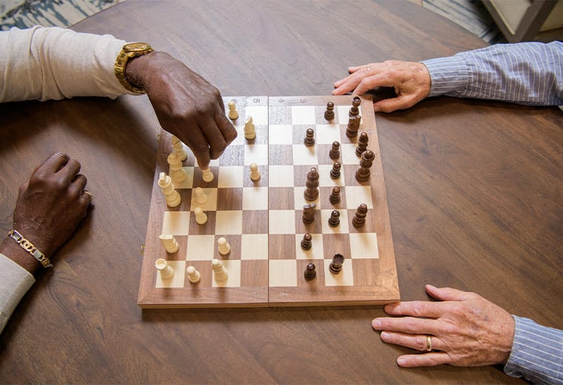A pair of hands are visible on either side of a wooden chess board