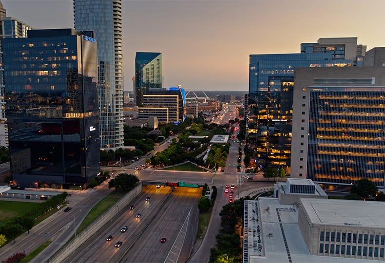 Aerial shot of Dallas on a summer evening, looking along the Woodall Rodgers Freeway (Spur 366) where it passes beneath Klyde Warren Park.