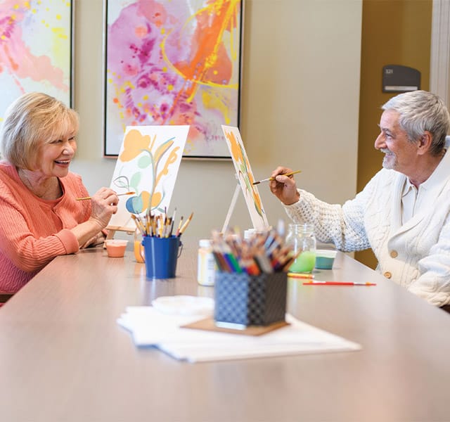 Residents sitting at a table painting with water colors.