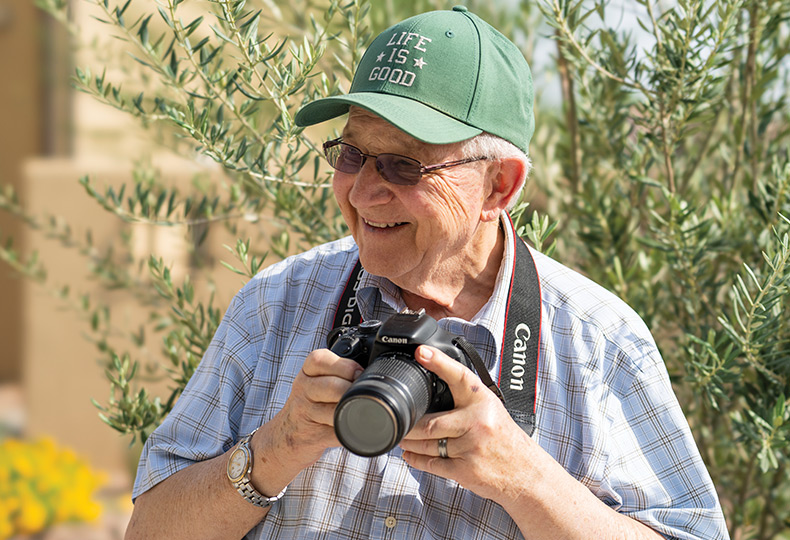 A resident in green hat holding a camera outside and smiling